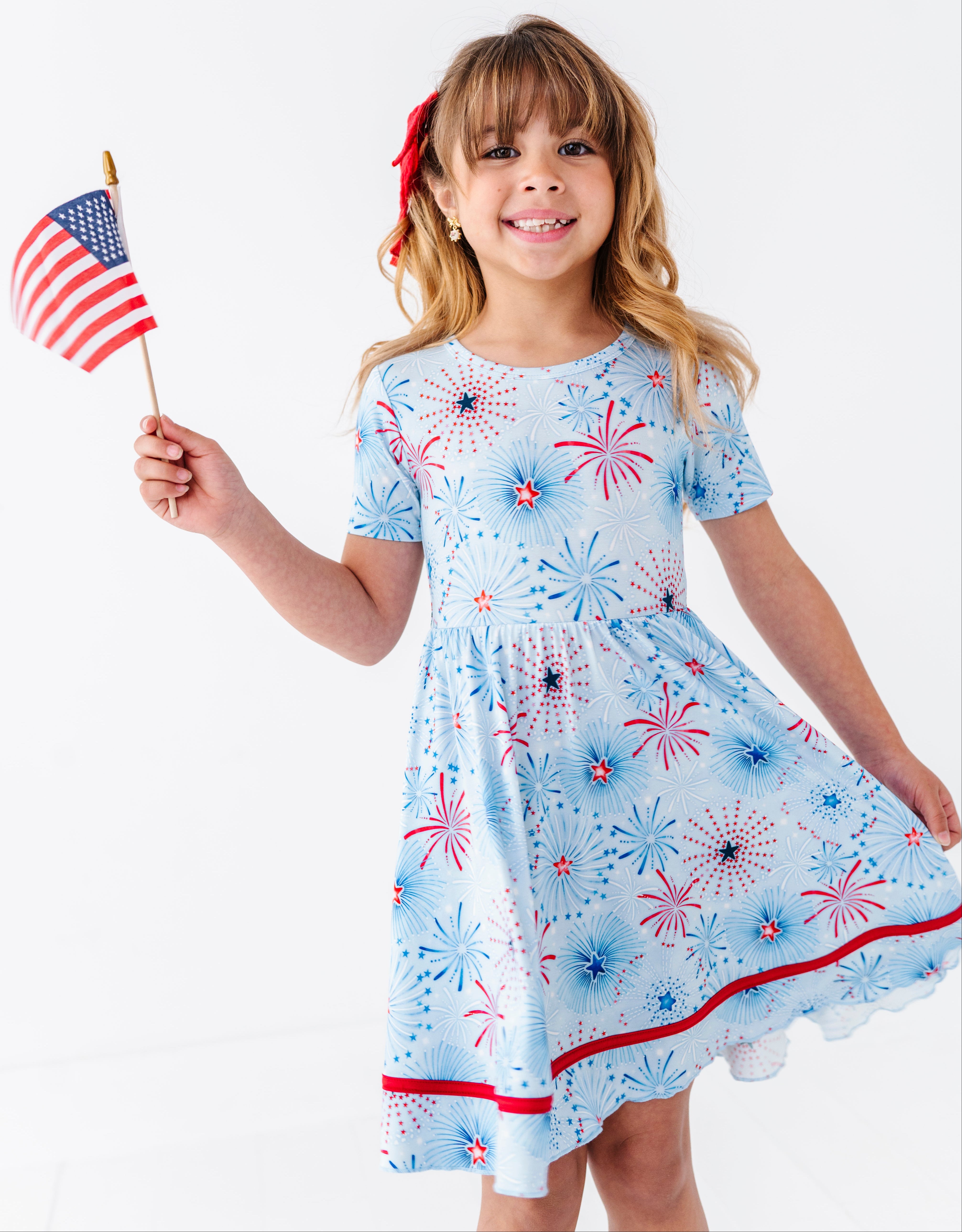 Young girl wearing a patriotic bamboo twirl dress, holding an American flag.
